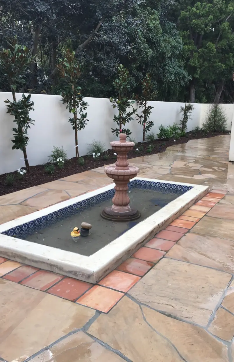 After: a flagstone courtyard with a tiled fountain and new planting along the wall