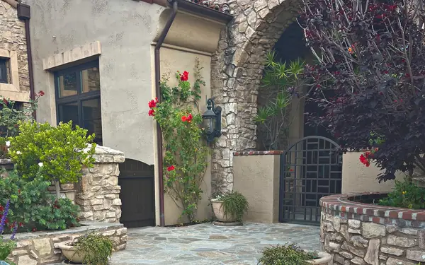 A stone archway and iron gate beside climbing red roses on a flagstone courtyard